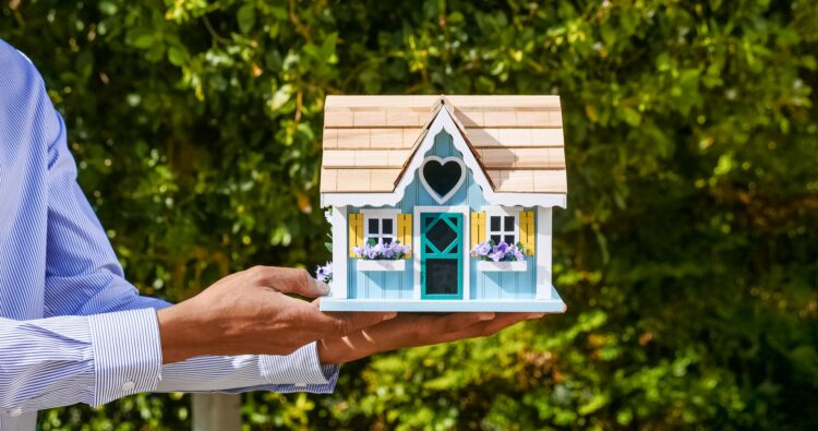 Professionnel de l'immobilier tenant une maison de poupée, symbolisant à quel point il est facile d'acheter et de vendre des maisons avec des iBuyers